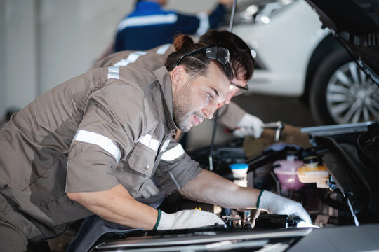 Professional electric vehicle technician performing inspection and maintenance inside the engine compartment of an EV at a modern automotive service workshop, ensuring vehicle safety, performance.
