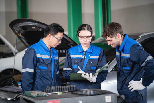 Professional automotive technicians reviewing inspection records and maintenance procedures for an electric vehicle while collaborating in a modern repair workshop.