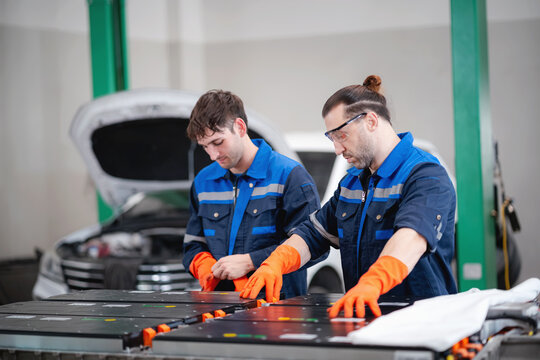 Professional automotive technicians inspecting a high-voltage electric vehicle battery pack during maintenance and diagnostic procedures in a modern EV service workshop.