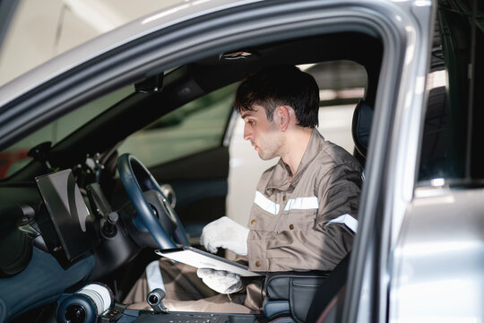 Professional electric vehicle technician operating a digital tablet to perform vehicle diagnostics, software inspection, and maintenance procedures inside an electric car.
