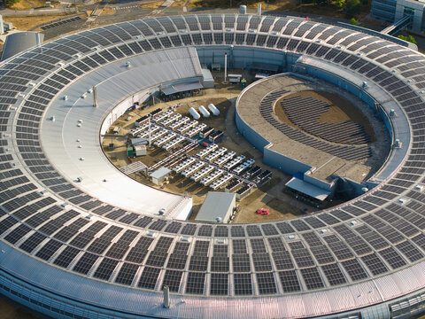 Aerial view of the Diamond Light Source synchrotron facility with its circular design, rooftop solar panels, and technical equipment in Harwell Oxford, England, United Kingdom.