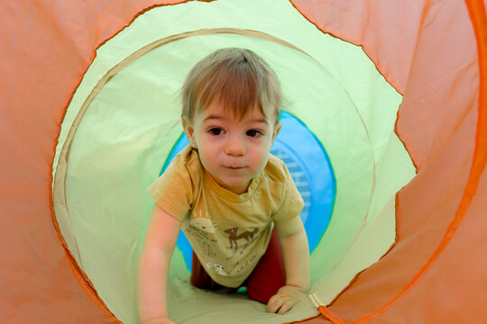 Toddler crawl through colorful play tent tunnel indoors