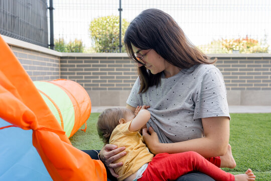 Mother breastfeed baby beside play tent on artificial grass
