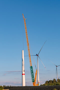 Heavy crawler crane assembling wind turbine tower under clear blue sky at wind farm, renewable green energy construction concept