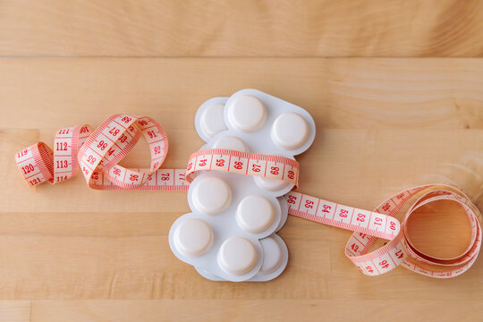 Weight Loss Pills with Measuring Tape on Wooden Background, Diet Supplement and Slimming Concept