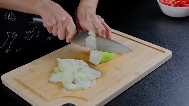 A person in a dark shirt slices green and white onions on a wooden cutting board with a silver knife in a bright kitchen in Cooking.