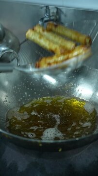 Vertical video close up of chef tossing deep fried golden spring rolls in wire skimmer strainer over oil kadhai