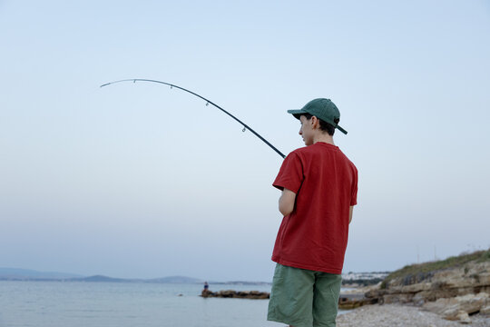 Teenager fishing with rod on rocky coast at dusk