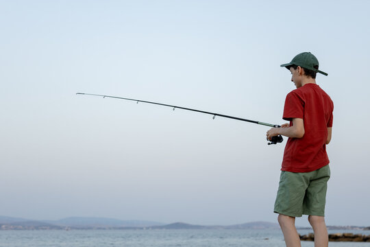 Teenager fish with rod by sea under cloudy sky