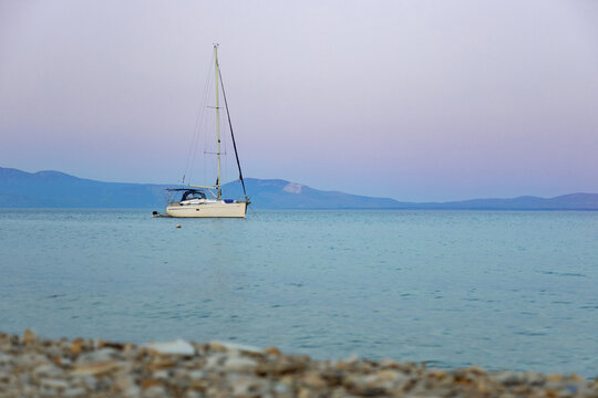 Sailboat anchored on calm sea beneath distant mountain range