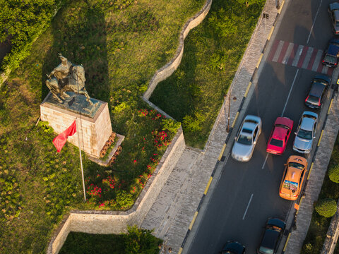 Aerial view of the Skanderbeg monument on horseback with a red flag and surrounding greenery next to a road with traffic in Kruje, Durres County, Albania.