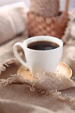 Cup of coffee stands against background of balls of yarn. Skeins of yarn are in basket. Beige wool yarn is out of focus. Hobby concept