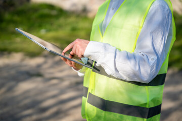 Obraz premium Engineer using tablet computer on construction site wearing safety vest. Digital workflow mobile construction documentation and engineering tools