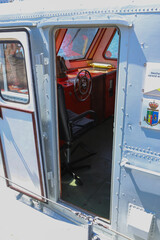 View through open door into a ship's wheelhouse with steering wheel, captain's chair, and control panel. © Ilia