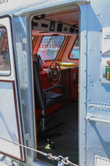 View through open doorway into the captain cabin and wheelhouse of a small boat with steering wheel and chair © Ilia