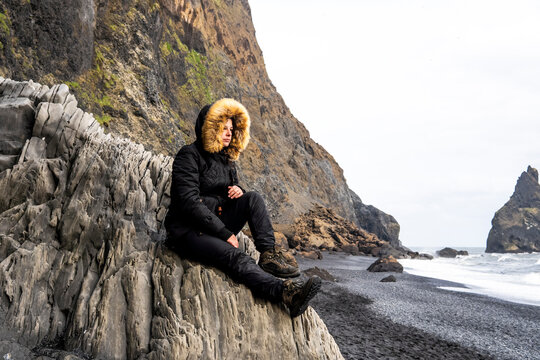 Traveler in fur hood on Iceland black sand beach