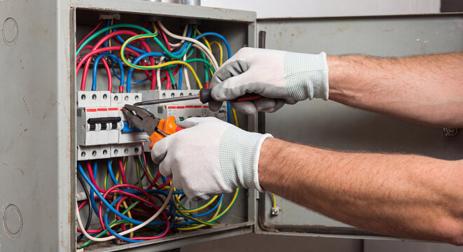 An electrician wearing protective gloves carefully connects and installs wires inside an electrical panel.