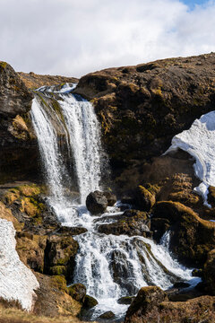 Waterfall and snow in Icelandic mountain landscape