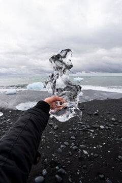 Hand holding iceberg crystal on Iceland black sand beach