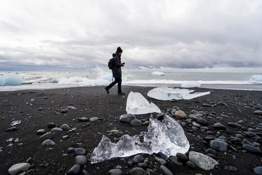 Traveler walks along Iceland black sand beach with icebergs