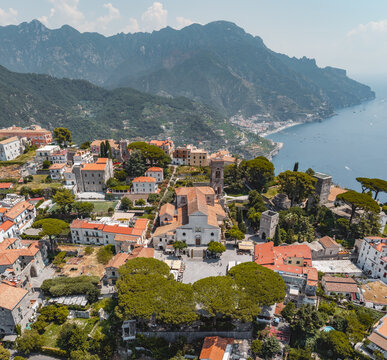 Aerial view of Ravello Cathedral surrounded by historic terracotta rooftops, lush pine trees, and the Mediterranean Sea in the background in Ravello, Amalfi Coast, Italy.