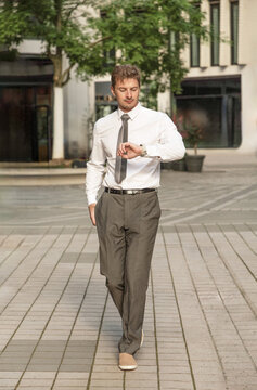 Young businessman check wristwatch while walk in city