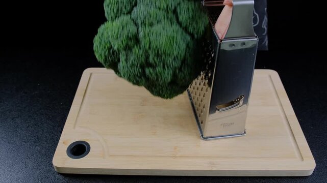 Adult hands chop fresh broccoli using an electric mini chopper on a wooden cutting board in a Cooking kitchen during daytime.