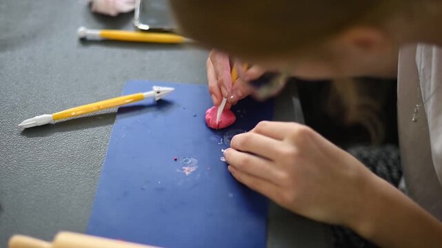 Young artisan sculpting a small pink figurine from polymer clay using modeling tools in a creative workshop studio