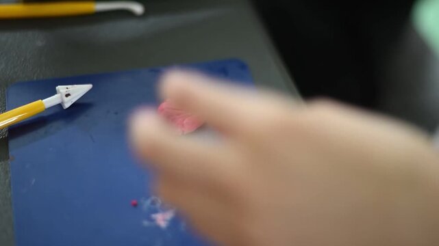 Young artisan sculpting a small pink figurine from polymer clay using modeling tools in creative workshop studio