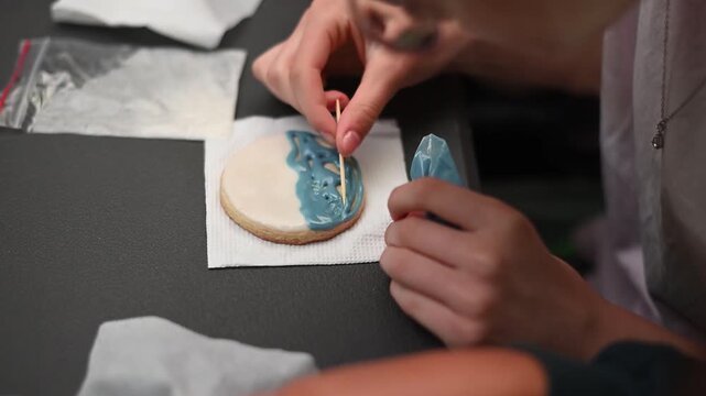 Professional pastry chef decorating cookie with blue royal icing and a toothpick a custom design