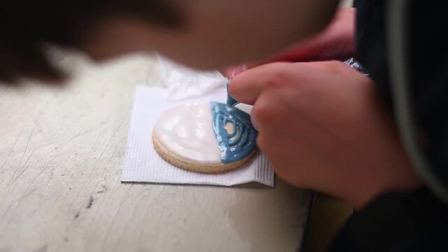 Professional pastry chef decorating cookie with blue royal icing and a toothpick custom design