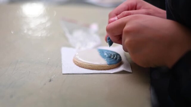 Professional pastry chef decorating cookie with blue royal icing and a toothpick for a custom design
