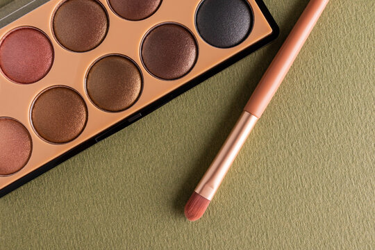 Autumn eyeshadow palette and makeup brush on olive background