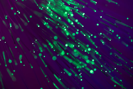 Green fiber optic light trails on purple technology background