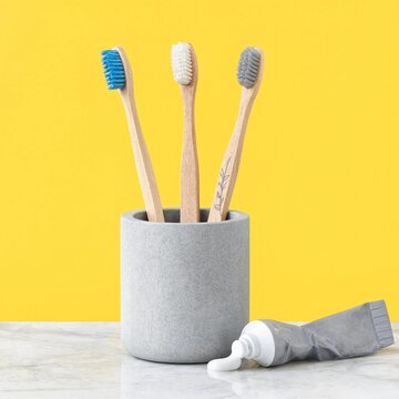 Three bamboo toothbrushes stand upright in a grey holder next to toothpaste on a marble surface