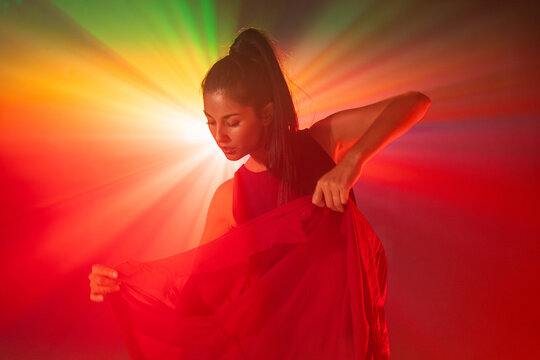 Latin woman dancer posing in red light with flowing fabric