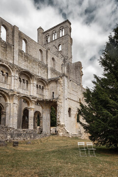 Ruins of Jumieges Abbey with Romanesque arches and empty chairs on lawn in Normandy, France