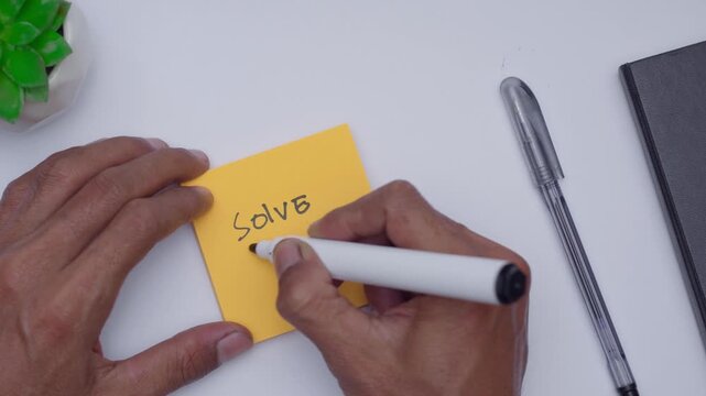 a man writing solve the problem on orange sticky note