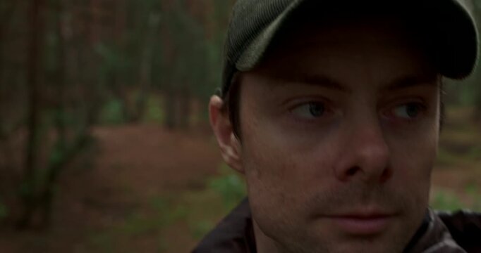 Close up portrait of man in cap walking through rainy forest