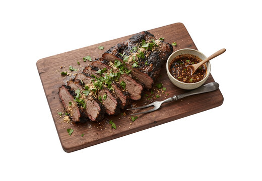 A wooden cutting board featuring grilled beef brisket served with Jaew sauce, set against a white background.
