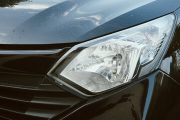 Shiny black car hood gleams under soft sunlight. Headlight reflects intricate internal structure clearly. Chrome trim glints against deep polished surface. Modern design exudes sleek © Mr. leo