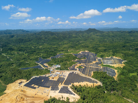 Aerial view of Sikatuna Solar Power Plant with rows of solar panels on cleared land surrounded by lush green hills and forests in Sikatuna, Central Visayas, Philippines.