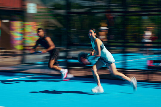 Stylish mixed padel pair running across court in coordinated sportswear with motion blur. Concept of couple activewear campaign, dynamic lifestyle fashion, sports partnership style.