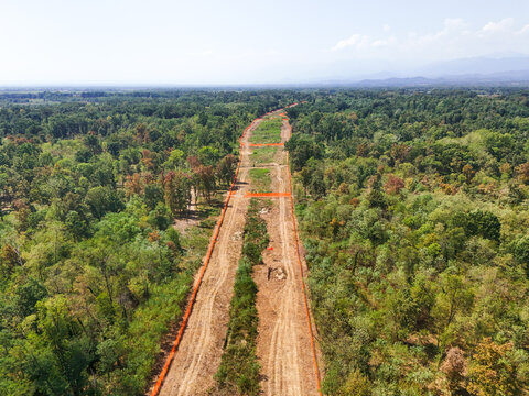 Aerial view of highway construction cutting through the Baraggia natural landscape with orange safety fencing and cleared land in Gattinara, Piedmont, Italy.