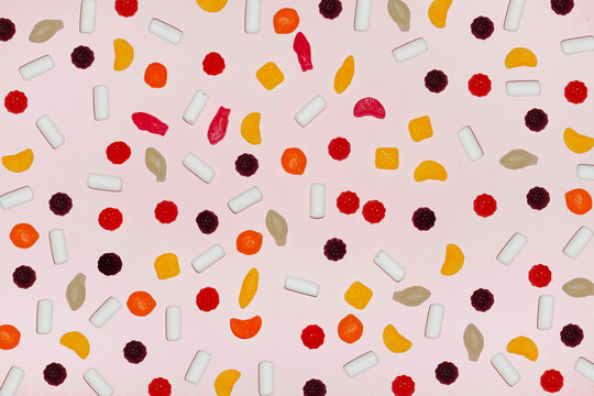 Colorful candy assortment on pastel pink background flat lay