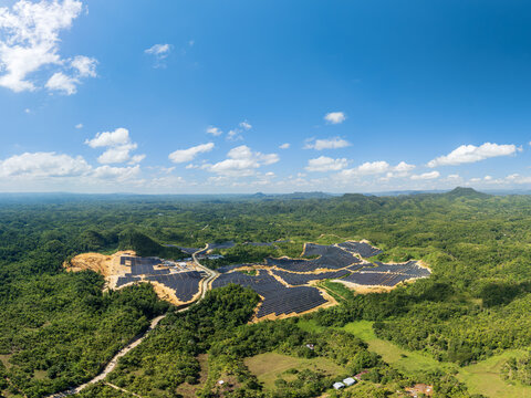 Aerial view of the Sikatuna Solar Power Plant featuring rows of photovoltaic panels set within a lush green landscape under a bright blue sky in Sikatuna, Central Visayas, Philippines.