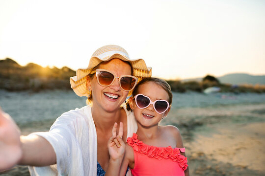 Mother and daughter smiling while taking a summer selfie at sunset on a sandy beach