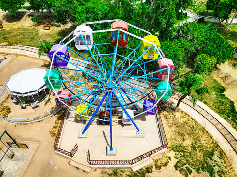 Aerial view of the colorful Ferris wheel at Kashmir Park, featuring vibrant gondolas surrounded by lush green trees and park pathways in Dera Ghazi Khan, Punjab, Pakistan.