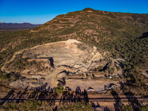 Aerial view of the Calcium quarry site, showing excavation pits, piles of crushed rock, heavy machinery, and surrounding forested hills in Calcium, Queensland, Australia.
