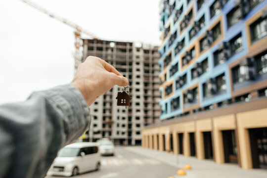 Man hold house key near new apartment building